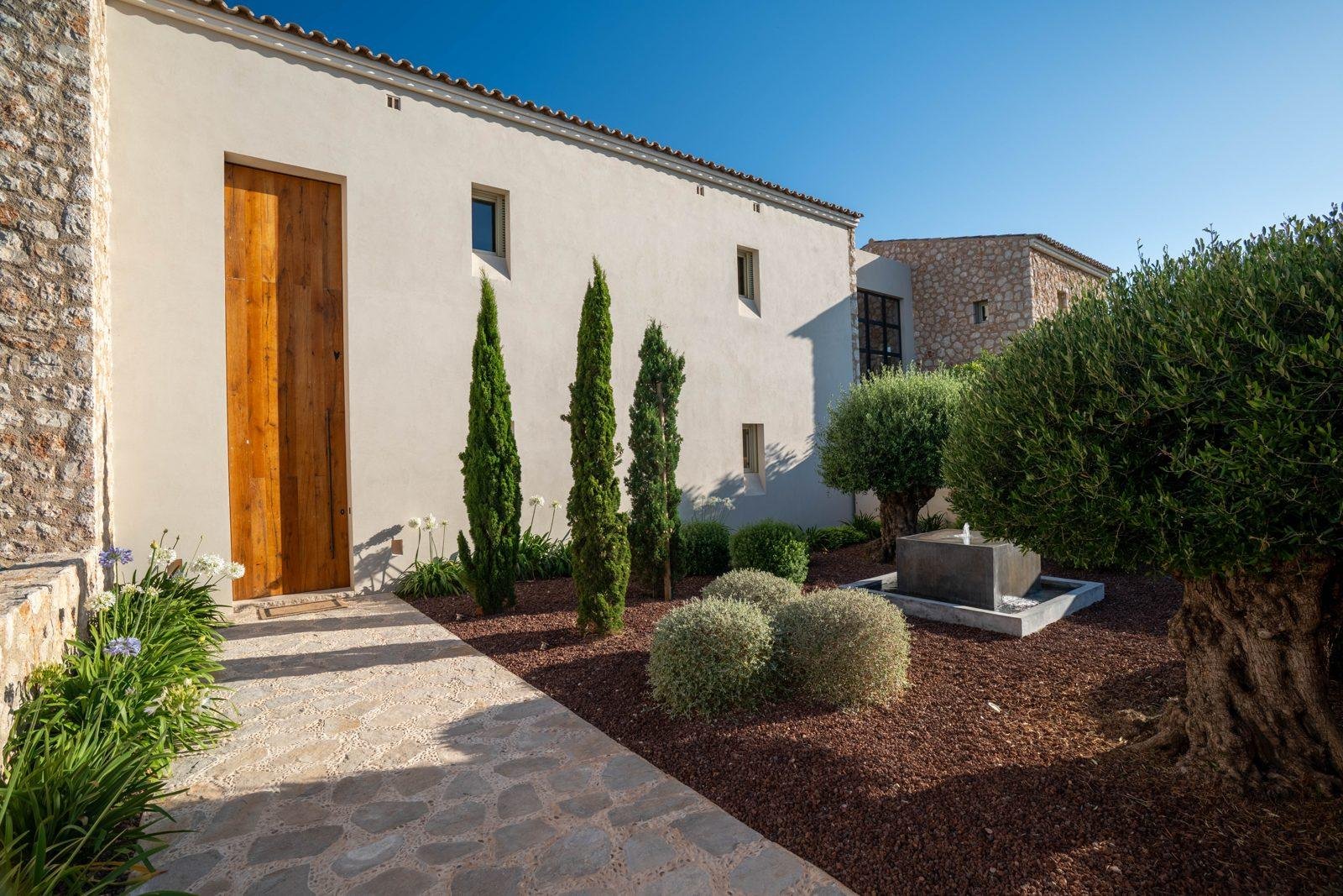Entrada de una casa con jardín de olivos y cipreses