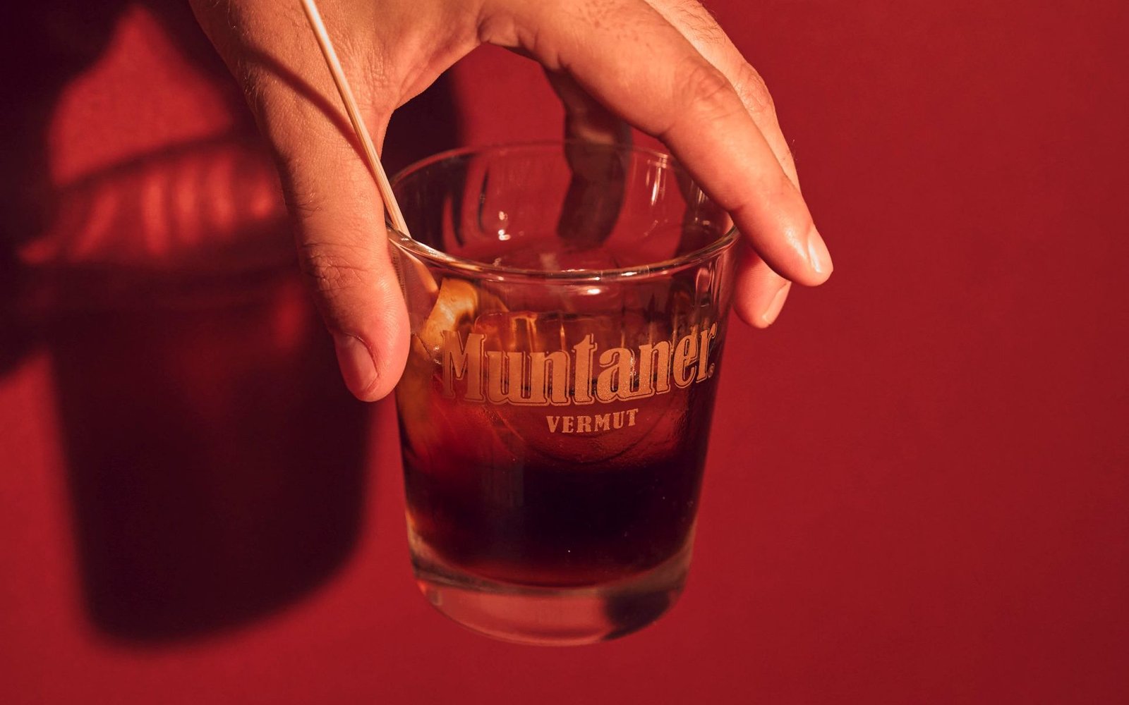 Mano sosteniendo un vaso de vermut Muntaner sobre fondo rojo