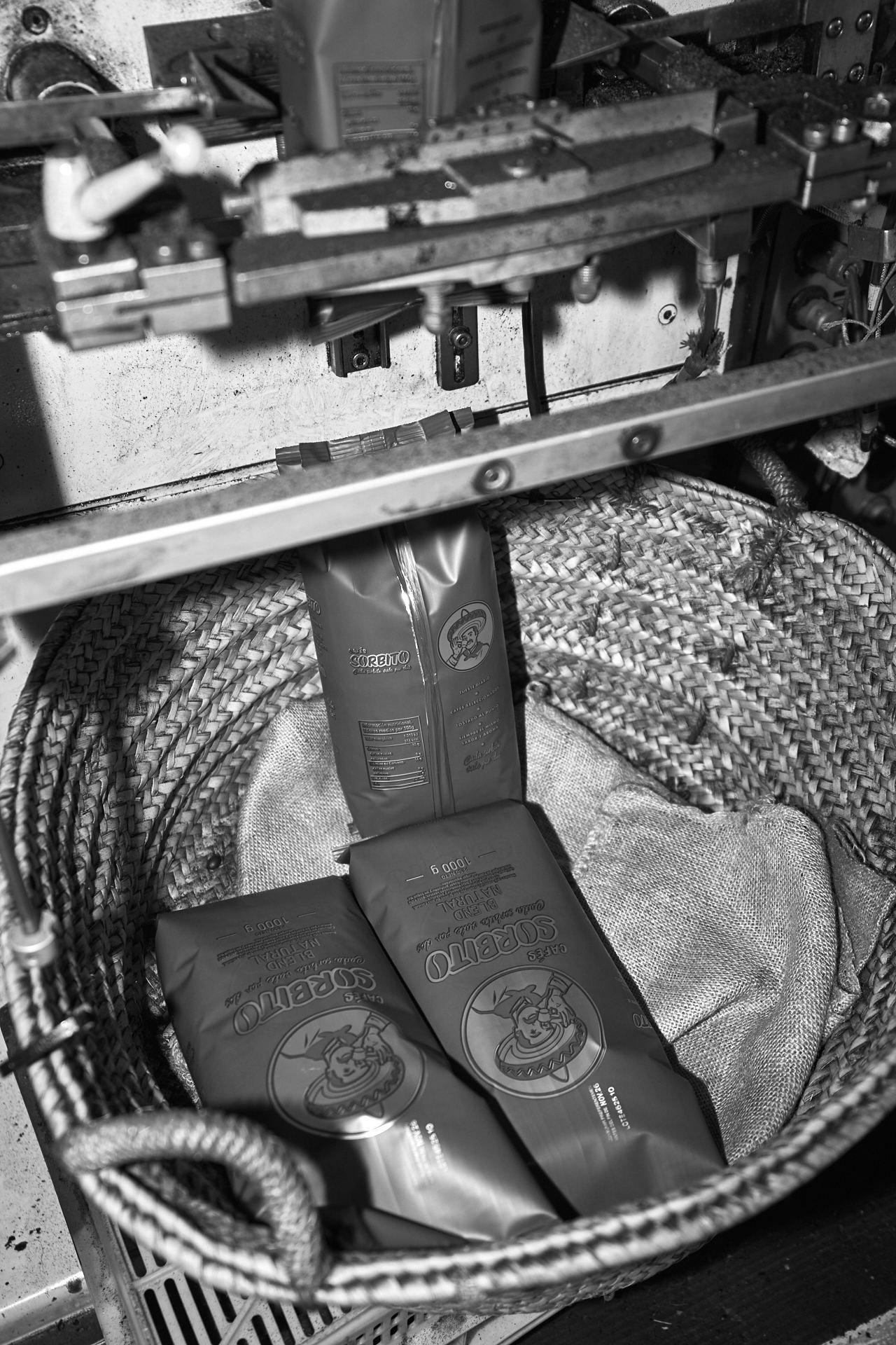 Paquetes de Cafés Sorbito recién envasados en una cesta, en blanco y negro