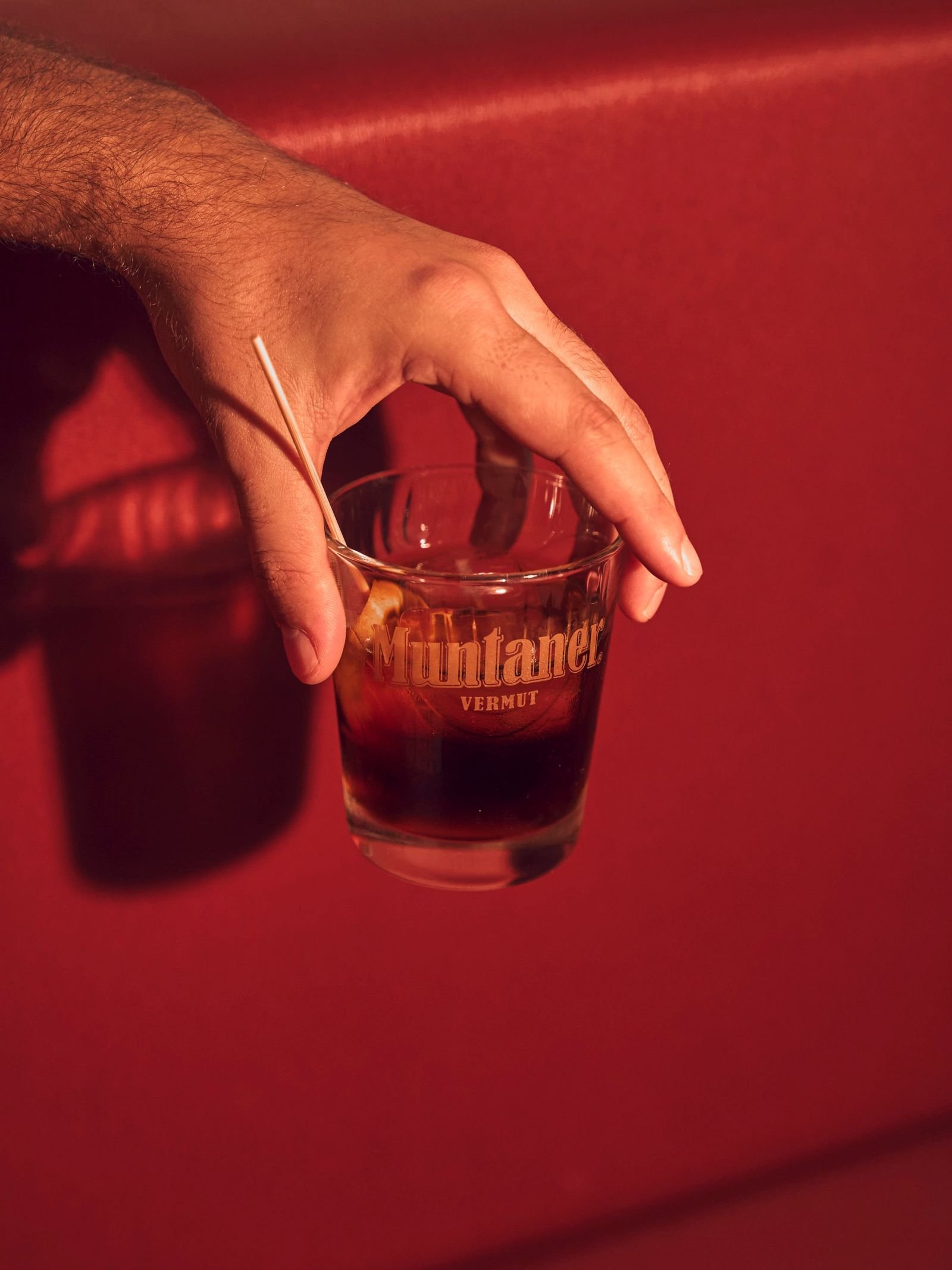 Fotografía de producto de vermut Muntaner en Mallorca: mano con vaso sobre fondo rojo