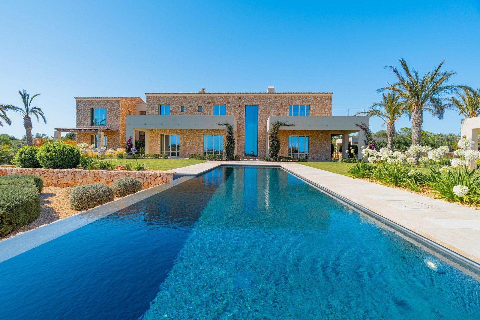 Villa de piedra con piscina desbordante y palmeras fotografiada en Mallorca